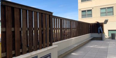 A person cleaning a tall wooden fence on a rooftop patio.