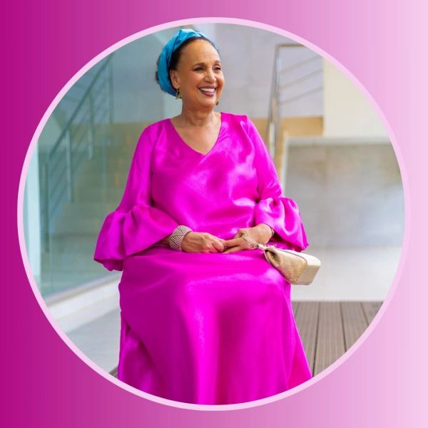 Elegant woman in bright pink dress and blue headscarf smiling gracefully.