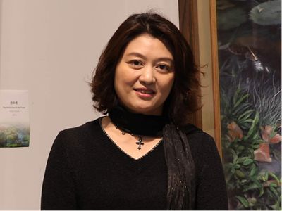 A woman in a black outfit and scarf smiling indoors.