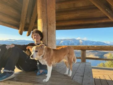 Person relaxing on a wooden deck with a dog and mountain view.