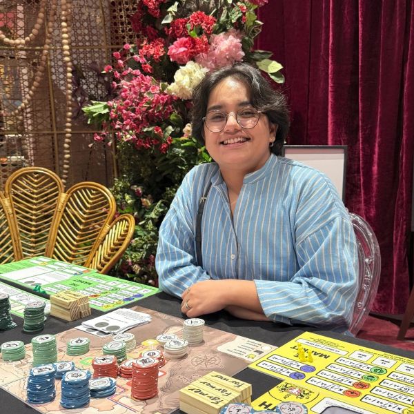 Person smiling playing a board game surrounded by flowers.