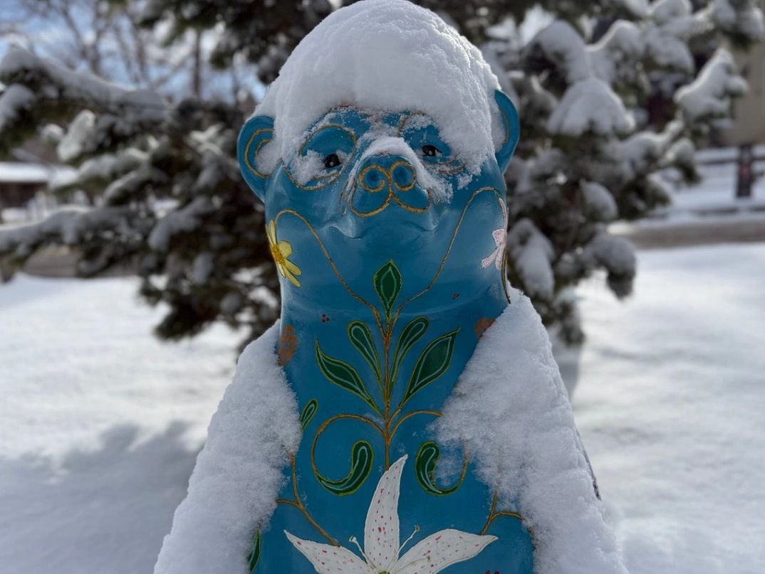 Snow-covered blue bear statue with floral patterns.