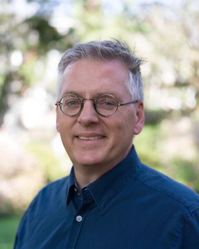 Middle-aged man with glasses smiling outdoors in a blue shirt.