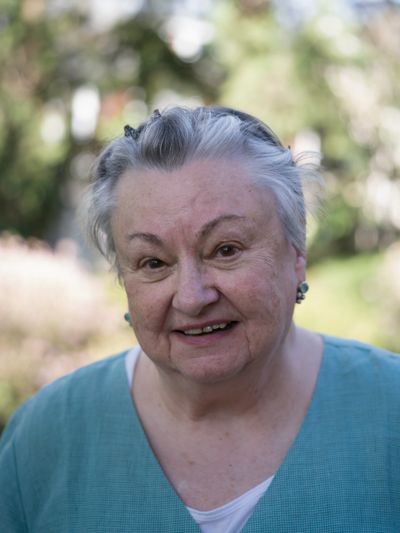 Smiling elderly woman with gray hair outdoors in a teal top.