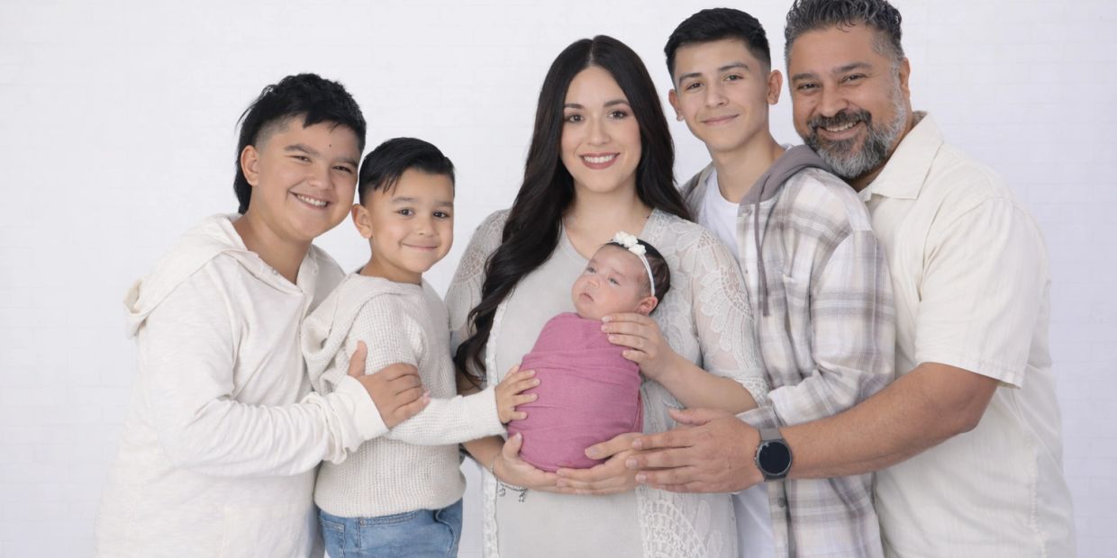 A happy family smiling together holding a newborn baby.