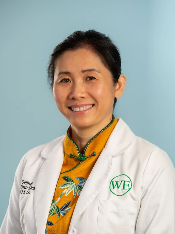 Professional woman in a white lab coat smiling against a light blue background.