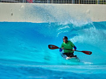 Person kayaking on a wave in a blue water pool.