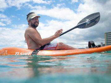 Man kayaking on a calm body of water under a cloudy sky.