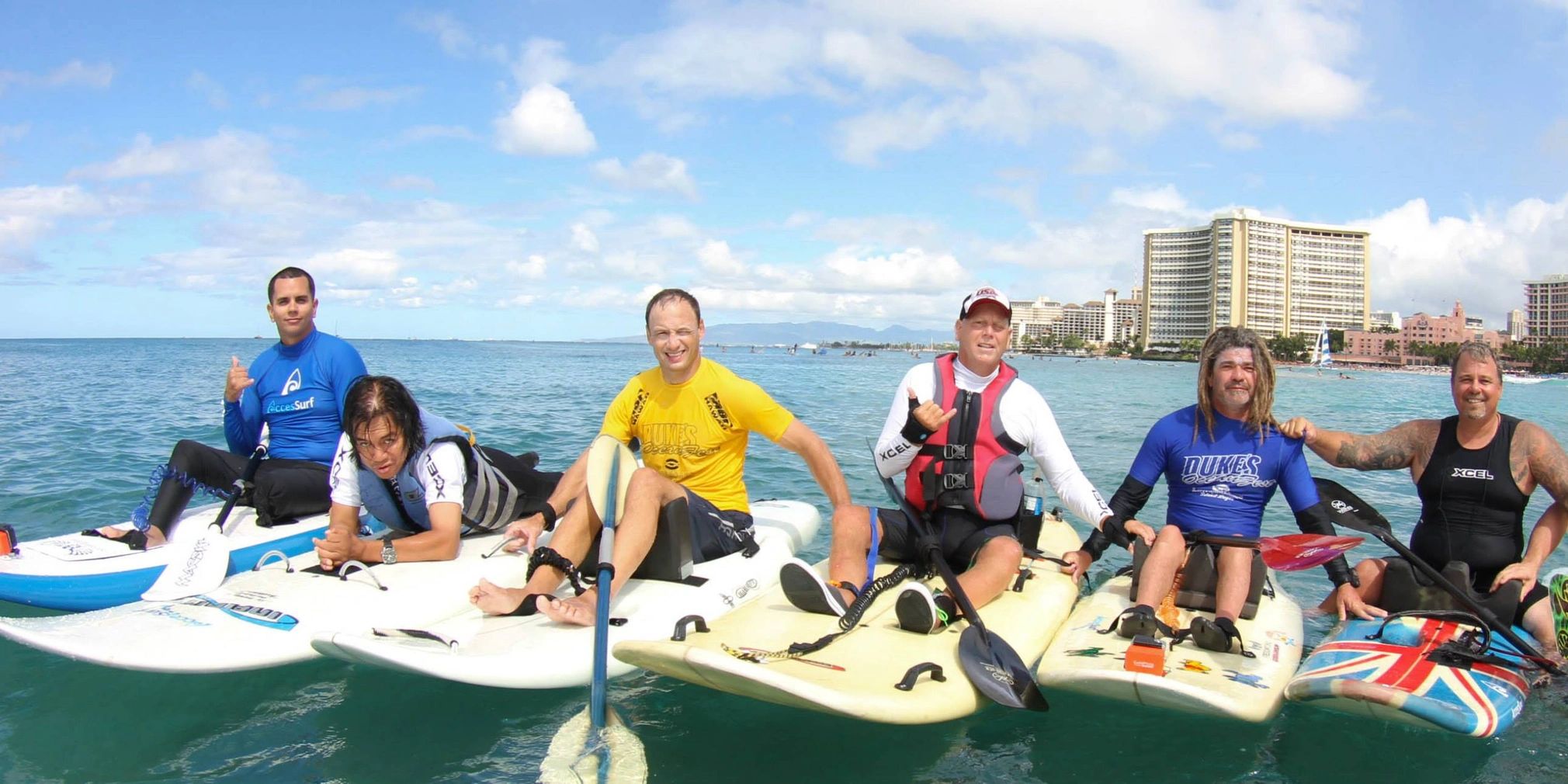 Group of six men on paddleboards enjoying sunny beach day.