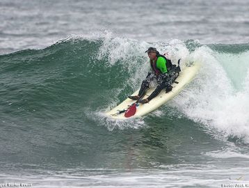 Surfer in green riding a wave on a white surfboard.