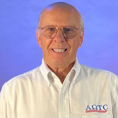 Smiling elderly man in glasses and white shirt with logo.
