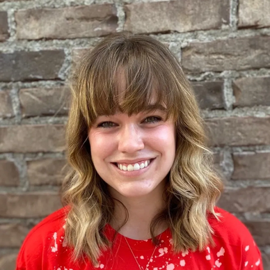 Smiling woman with wavy hair and bangs in red shirt.