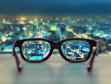 Glasses sitting on a ledge overlooking a city.  The city is blurry except for what is in the lens.