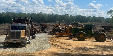 Heavy machinery and trucks at a logging site under a blue sky.