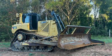 A large yellow Caterpillar bulldozer parked on dirt near trees.