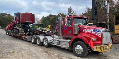 Red truck hauling heavy machinery on a trailer with an oversize load sign.