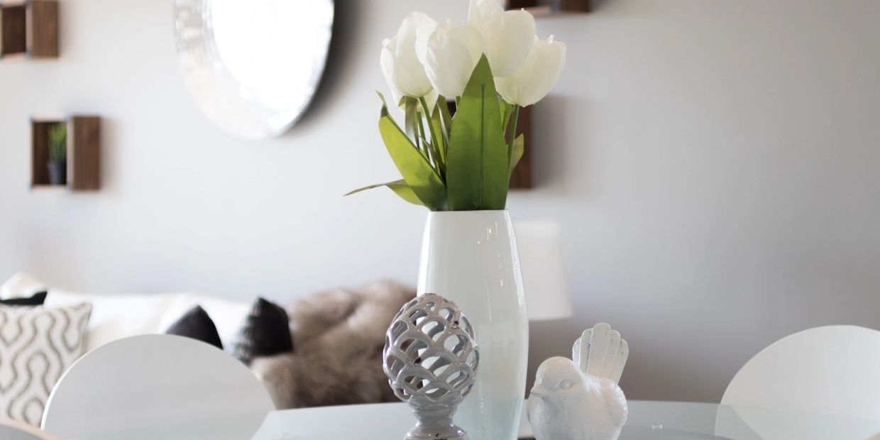 White flowers, a figure of a bird and an ornate egg resting on top of a table.