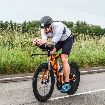 Cyclist racing on an orange and blue bike on a road.