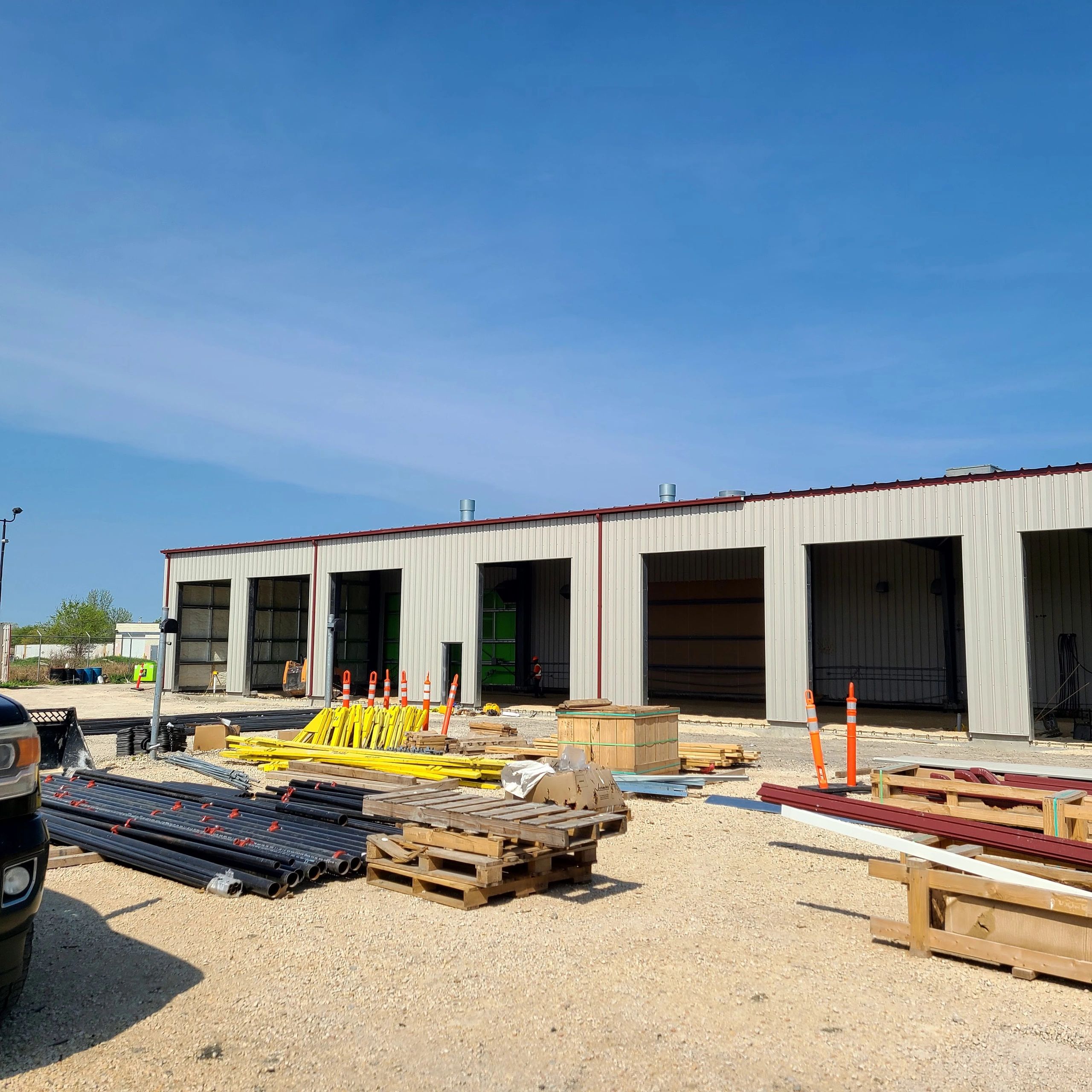 Exterior of an industrial building with construction materials and safety cones outside.