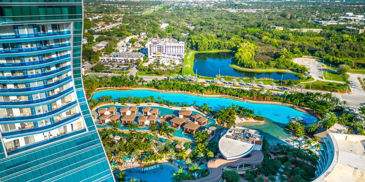 Aerial view of a resort with pools, cabanas, and a tall building.
