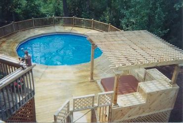 A large custom-built wooden pool deck with a pergola covering hot tub, detailed rails and trellises