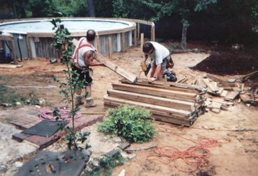Before photo of above-ground pool deck project.  Men prepping the wood for framing