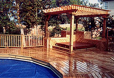 A large custom-built wooden pool deck with a pergola covering hot tub, detailed rails and trellises