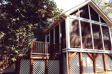 A screened addition with deck, stairs, and trellis under skirting. 