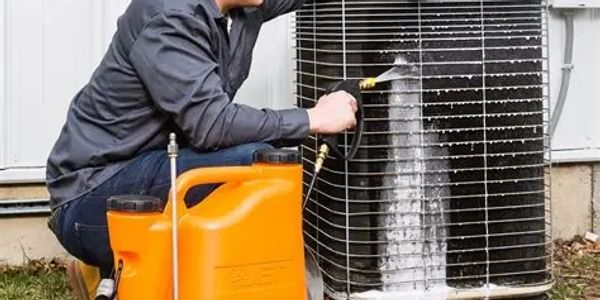 Technician cleaning an outdoor air conditioning unit with foam spray.