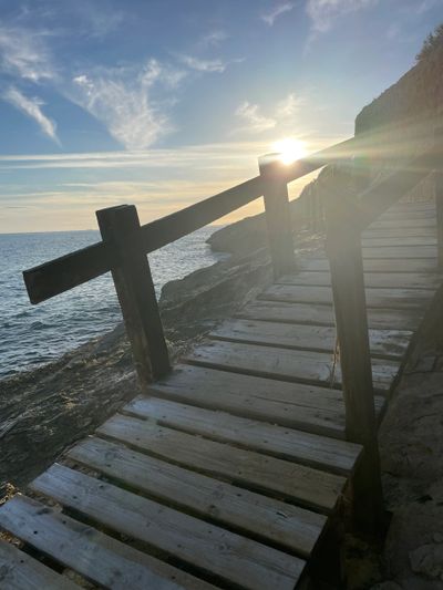 Wooden walkway along the rocky shore with the sun setting in the background.