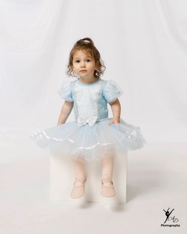 A young girl in a light blue dress sitting on a white block.