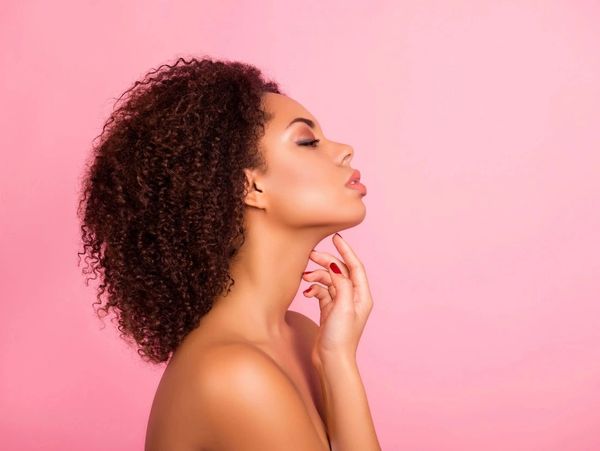 Woman touching neck, pink background.
