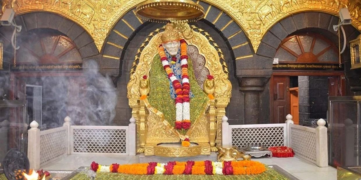 Statue adorned with garlands in a golden shrine with smoke and fire.
