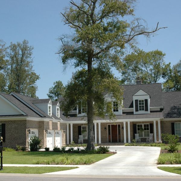Large brick house with porch, white columns, and mature tree.