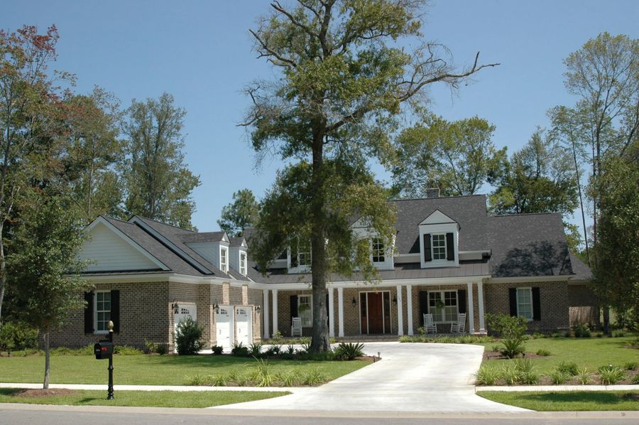 Large brick house with porch, white columns, and mature tree.