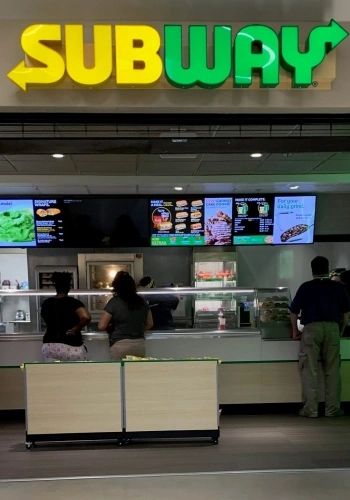 Subway restaurant counter with menu boards visible.