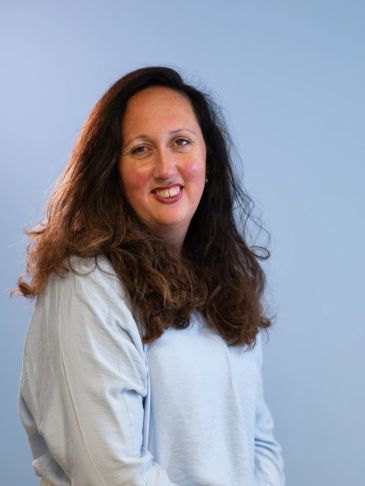 Vrouw met lang haar en lichtblauwe trui lacht naar de camera.