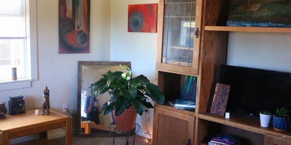 Cozy living room corner with plants, wooden furniture, and colorful paintings.