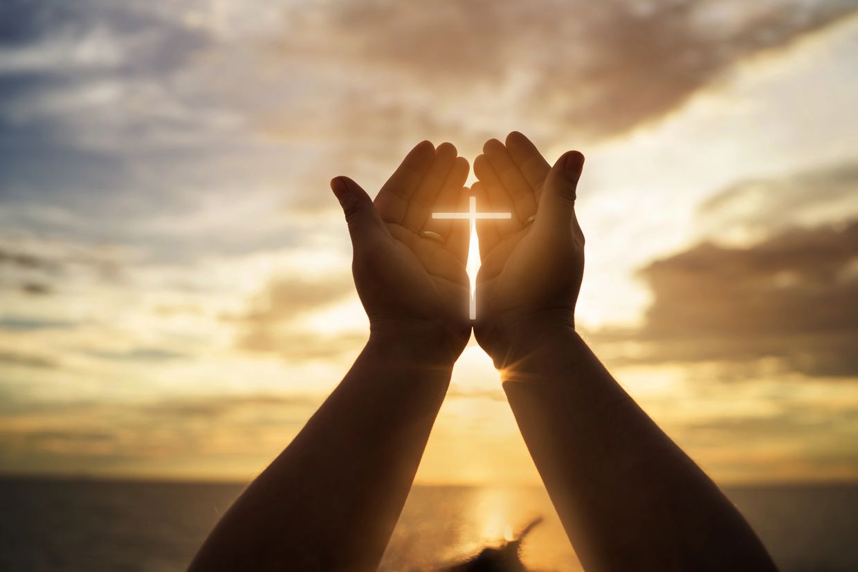 A Christian Cross sign in between two hands 