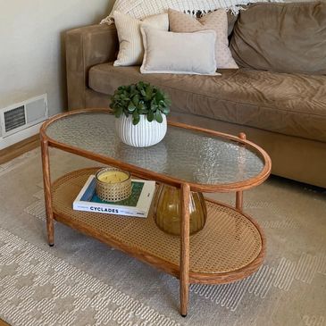 Oval light wood two layered coffee table with the bottom being rattan or woven and the top glass
