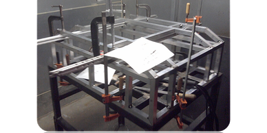 Metal frame structure being assembled with clamps and a blueprint on top.