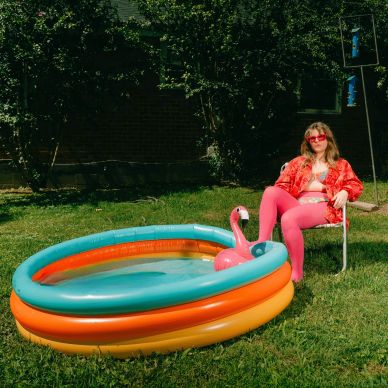 Person in bright pink outfit sitting by an inflatable pool with a flamingo float.