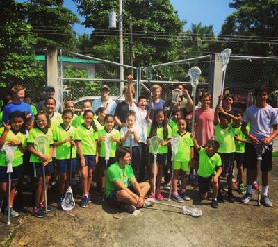 Youth lacrosse team posing outdoors with sticks under sunny sky.