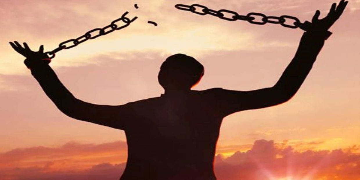 Silhouette breaking chains against sunset sky.