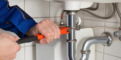 Person fixing a sink pipe with a wrench.