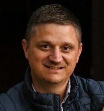 A man with short hair wearing a dark jacket smiles at the camera.