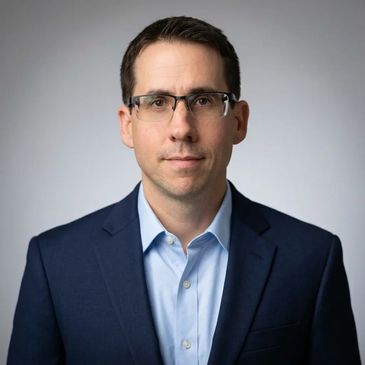 Professional man in glasses wearing a navy suit and light blue shirt.