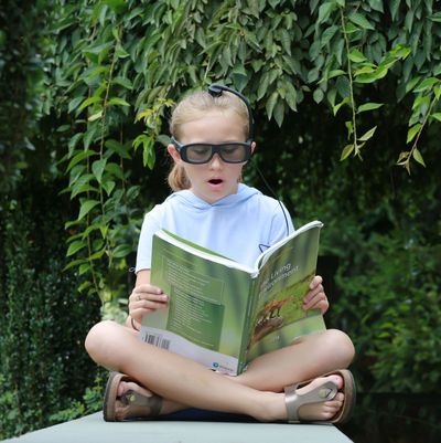 Girl with smart glasses reading an environment book outdoors.
