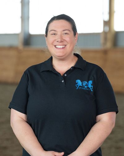 Smiling woman in a black polo shirt standing indoors.