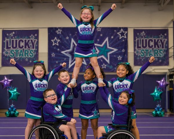 A diverse inclusive cheerleading team performing a stunt indoors.